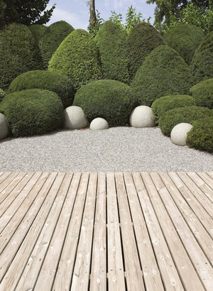 Übergang von Terrasse aus Holzbohlen auf angelegte glatte Kiesfläche. Im Hintergrund sind rund geschnittene Buchsbäume und runde Lichtkugeln