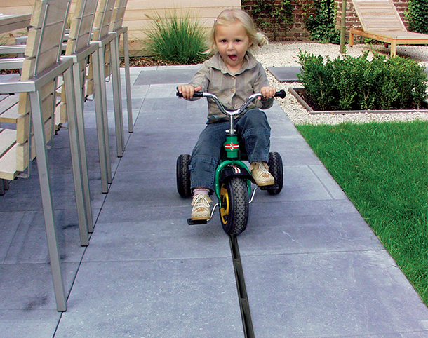Kind fährt mit dem Dreirad über die Terrasse über das kaum sichtbare Schlitzrost